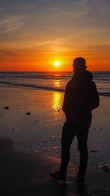 A model wearing a sky blue cap standing against a sunset beach backdrop.
