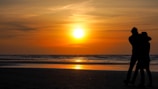 A sunset silhouette of two people embracing on a quiet beach.
