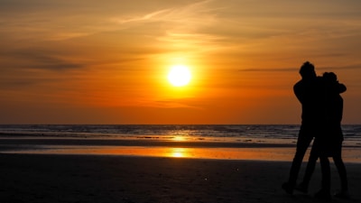A sunset silhouette of two people embracing on a quiet beach.