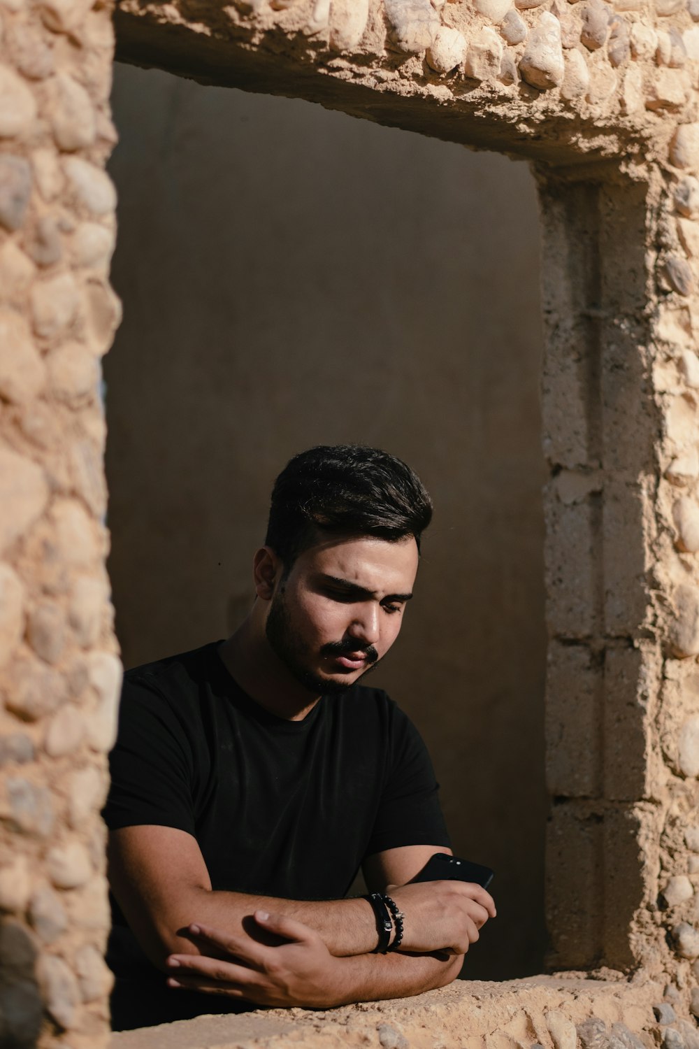 uomo in t-shirt girocollo nera seduto accanto al muro di cemento marrone