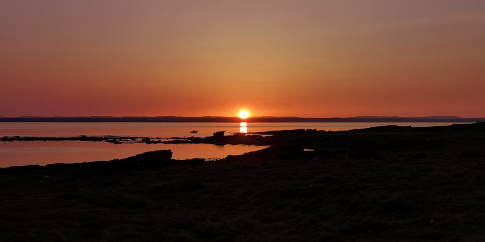 silhouette of person standing on seashore during sunset