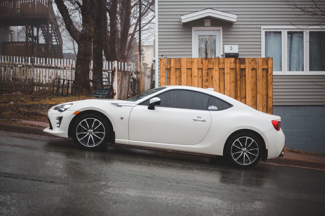 white porsche 911 parked near brown wooden fence during daytime