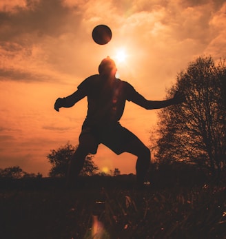 silhouette of man jumping on grass field during sunset