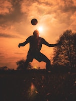 silhouette of man jumping on grass field during sunset