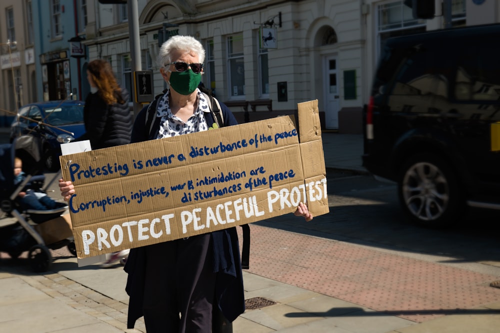 man in black coat holding blue and white signage