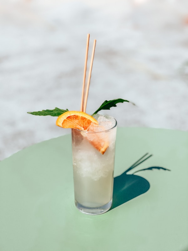 Clear drinking glass with white liquid and orange slice on green leaf