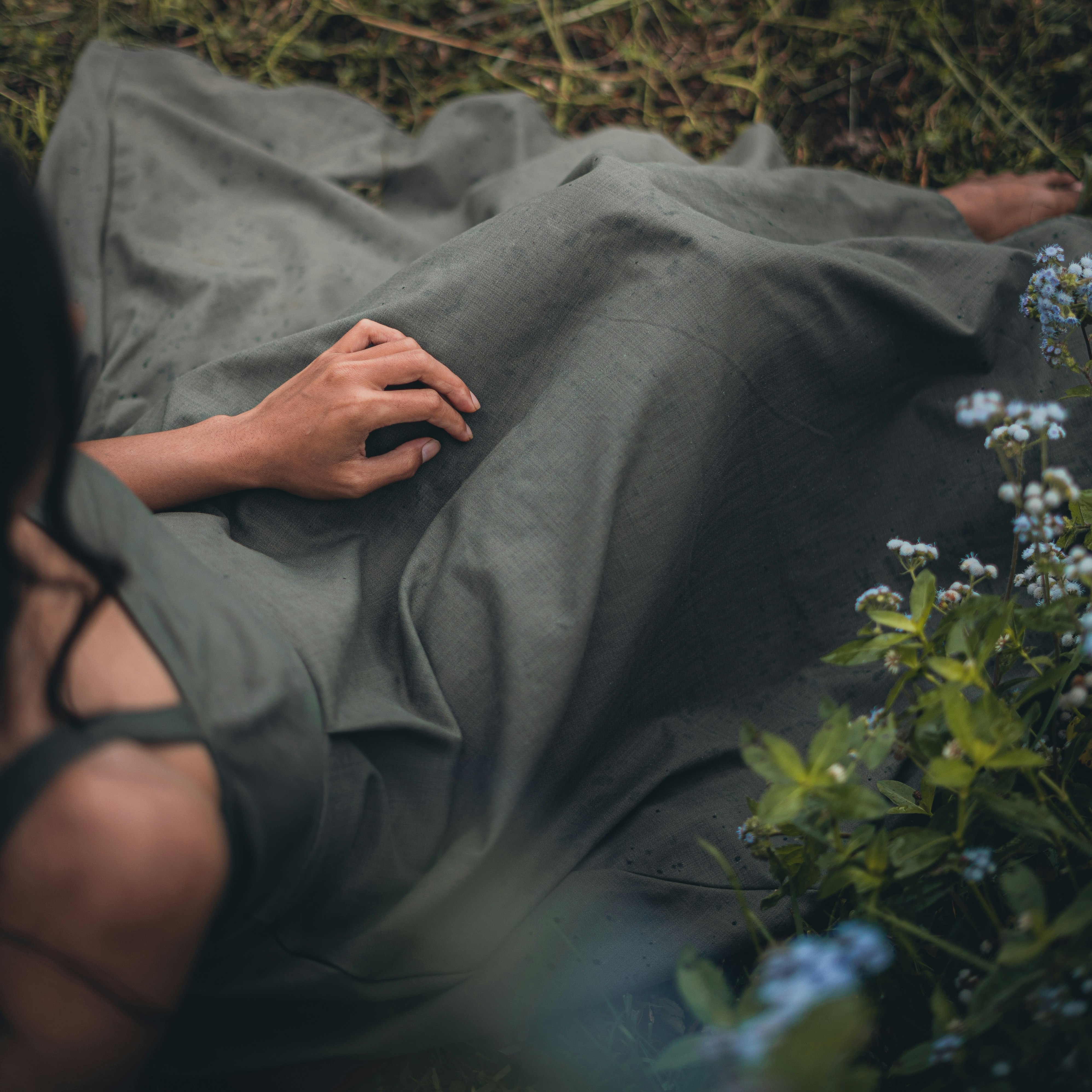 woman in gray shirt lying on ground covered with gray blanket