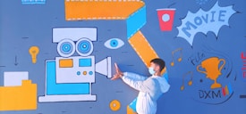 A person wearing a mask and white jacket poses in front of a vibrant mural. The mural includes a large vintage movie camera in blue and orange, an eye, a lightbulb, a cup, and a trophy labeled 'Film DXM'. Musical notes and the word 'MOVIE' are also part of the design.