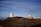A clear view of an astronomical observatory with multiple large telescopic domes situated on a rocky, elevated terrain. The sky above is overcast with wispy clouds, and the road winding through the site leads up to the domes.