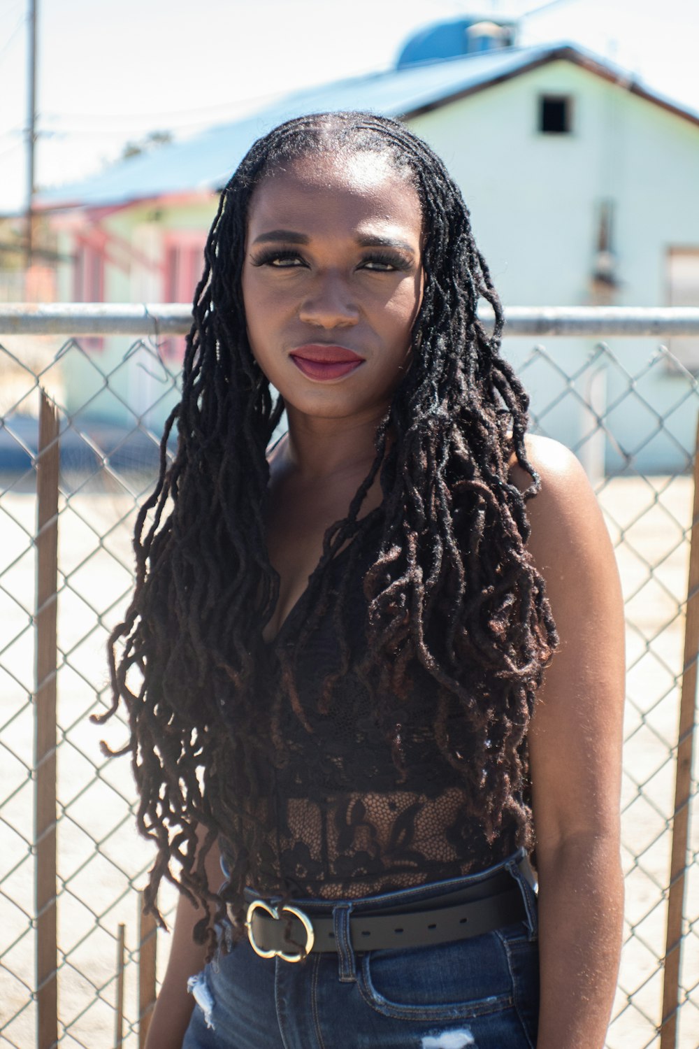 woman in black and brown sleeveless top leaning on chain link fence during daytime