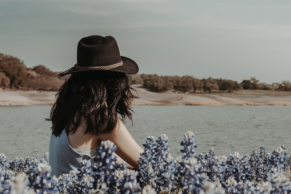 woman in blue and white floral shirt wearing brown hat standing on brown sand near body