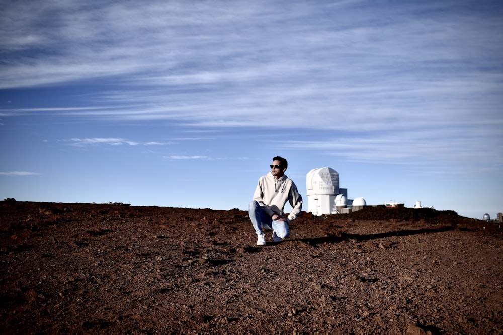 man in white dress shirt and blue denim jeans sitting on brown ground during daytime