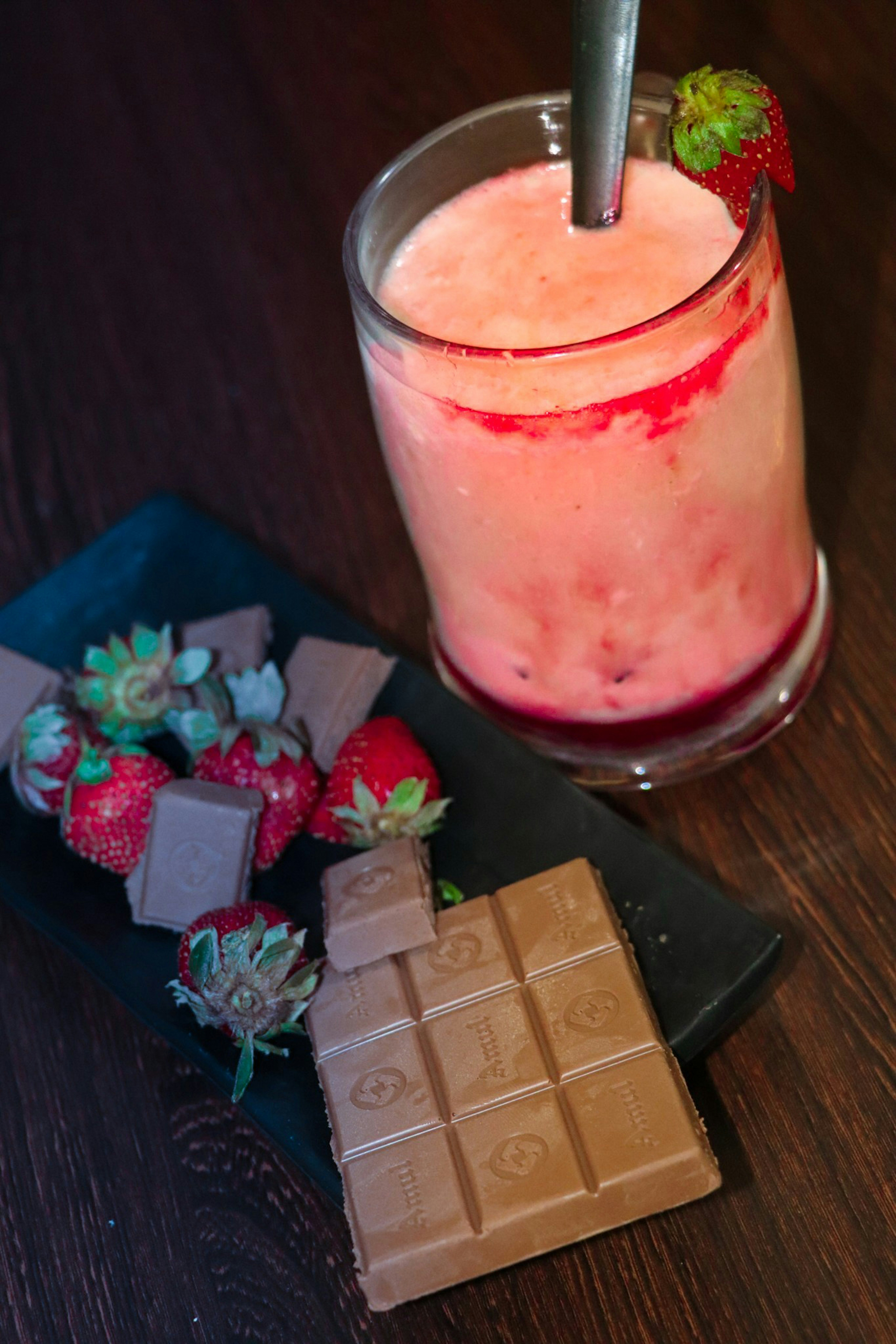 Tall glass strawberry milkshake with whipped cream and fresh strawberry garnish, dark moody background