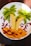 A creative fruit arrangement on a white plate, resembling a tropical scene. Slices of bananas form palm tree trunks, while kiwi slices act as the leaves. Orange segments create a sandy beach effect, surrounded by scattered pomegranate seeds that add a vibrant contrast.