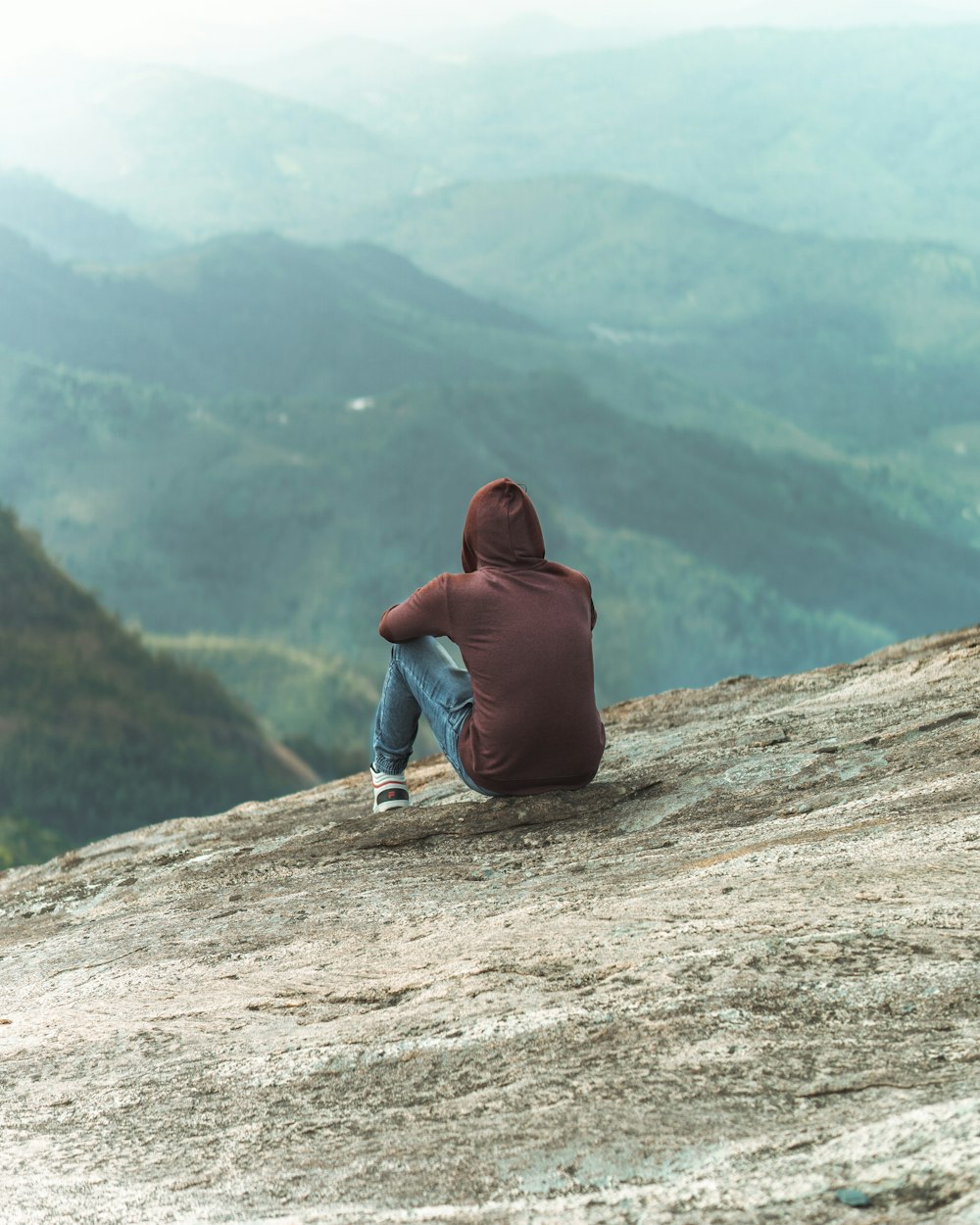 woman in blue hoodie and blue denim jeans sitting on brown rock mountain during daytime