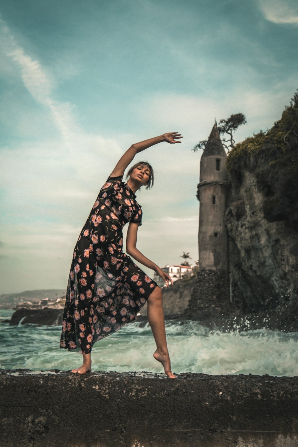 woman in black and white floral dress standing on rock formation near body of water during