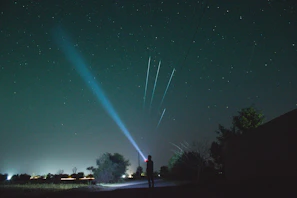 A professional astronomer pointing out constellations to children using a laser pointer in a dark garden.