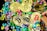 A collection of gold coins featuring the Bitcoin logo is scattered among colorful gemstones. The coins have black, red, and gold bitcoin symbols, while various hands can be seen interacting with them.
