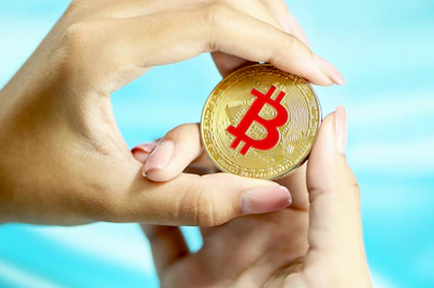 Close-up of hands holding a golden bitcoin coin against a dark background.