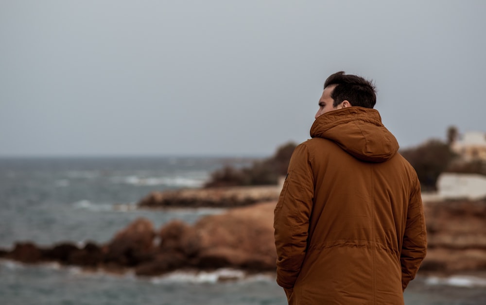 man in brown hoodie standing near body of water during daytime