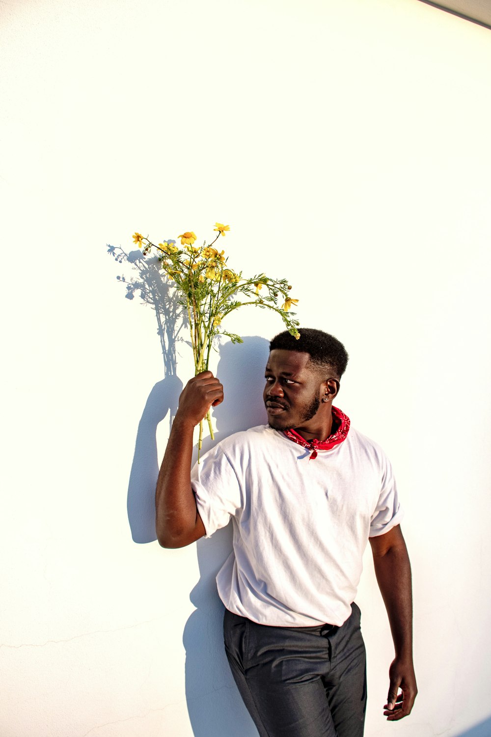 man in white crew neck t-shirt holding yellow flower