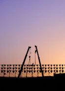 Technician welding a crane boom on a busy construction site at sunset.