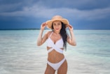 woman in white bikini wearing brown sun hat standing on beach during daytime