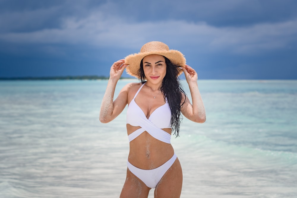 mulher no biquíni branco que usa o chapéu de sol marrom em pé na praia durante o dia