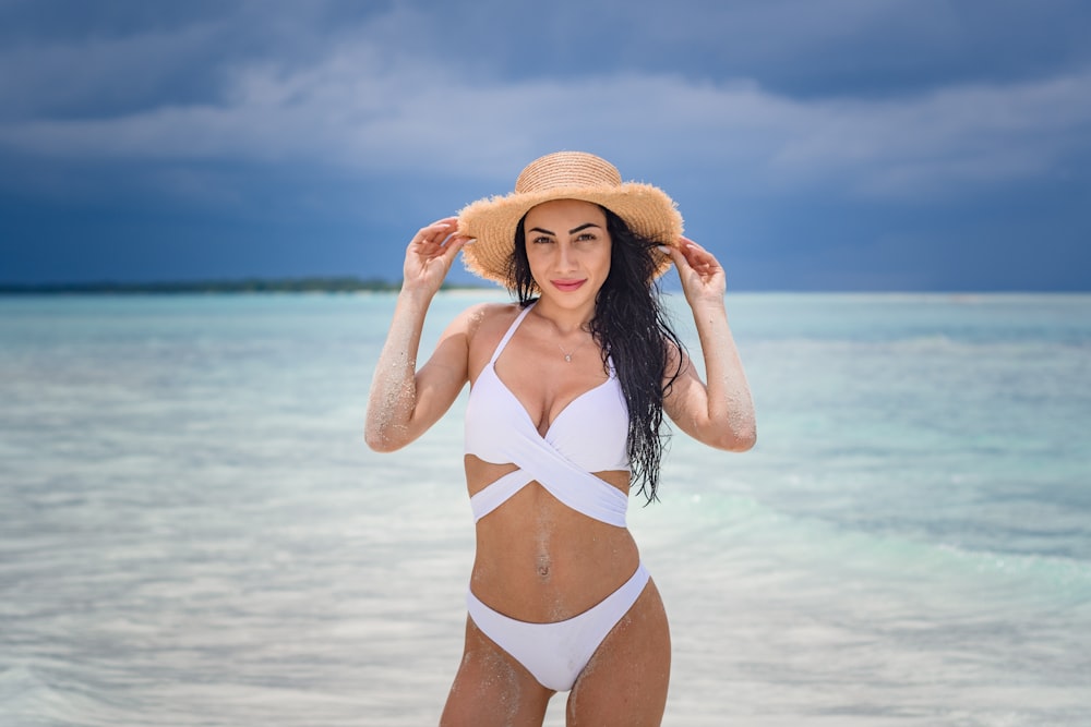 Mujer en bikini blanco con sombrero marrón para el sol de pie en la playa durante el día