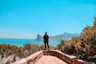 man in black jacket standing on brown concrete pathway near body of water during daytime