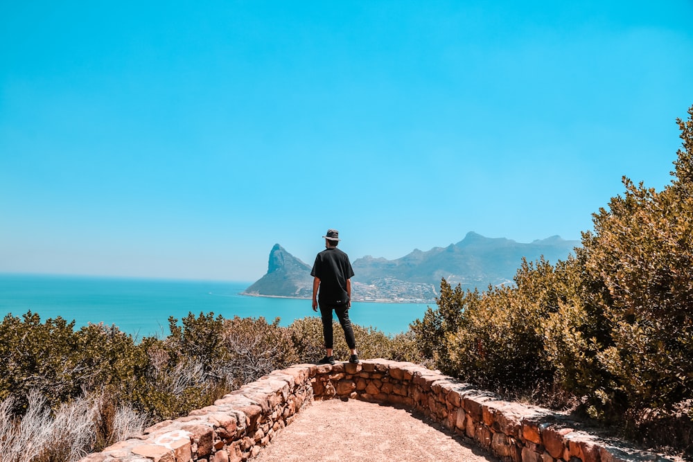 man in black jacket standing on brown concrete pathway near body of water during daytime