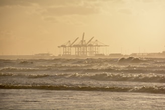Sky-high perspective of a coastline with waves gently hitting the shore near industrial docks.