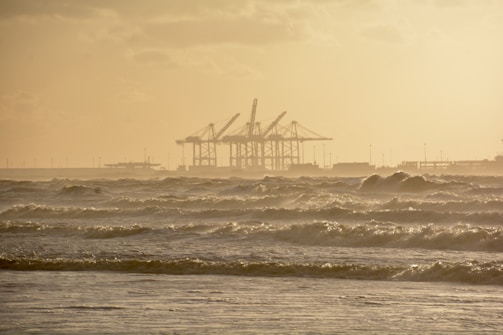 Sky-high perspective of a coastline with waves gently hitting the shore near industrial docks.