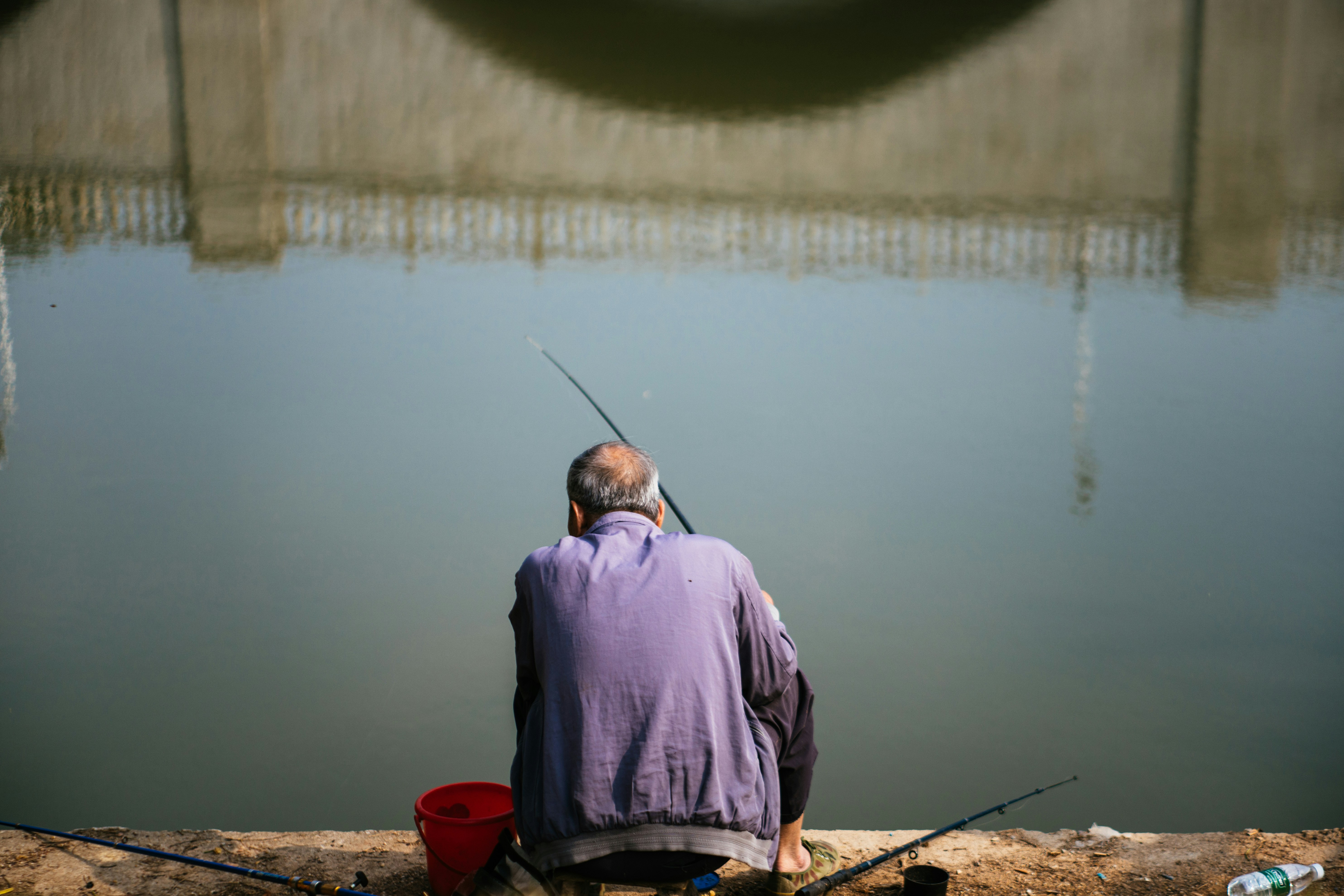 man in purple dress shirt and black pants sitting on brown wooden dock during daytime