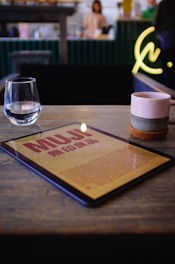 red book beside clear drinking glass on brown wooden table
