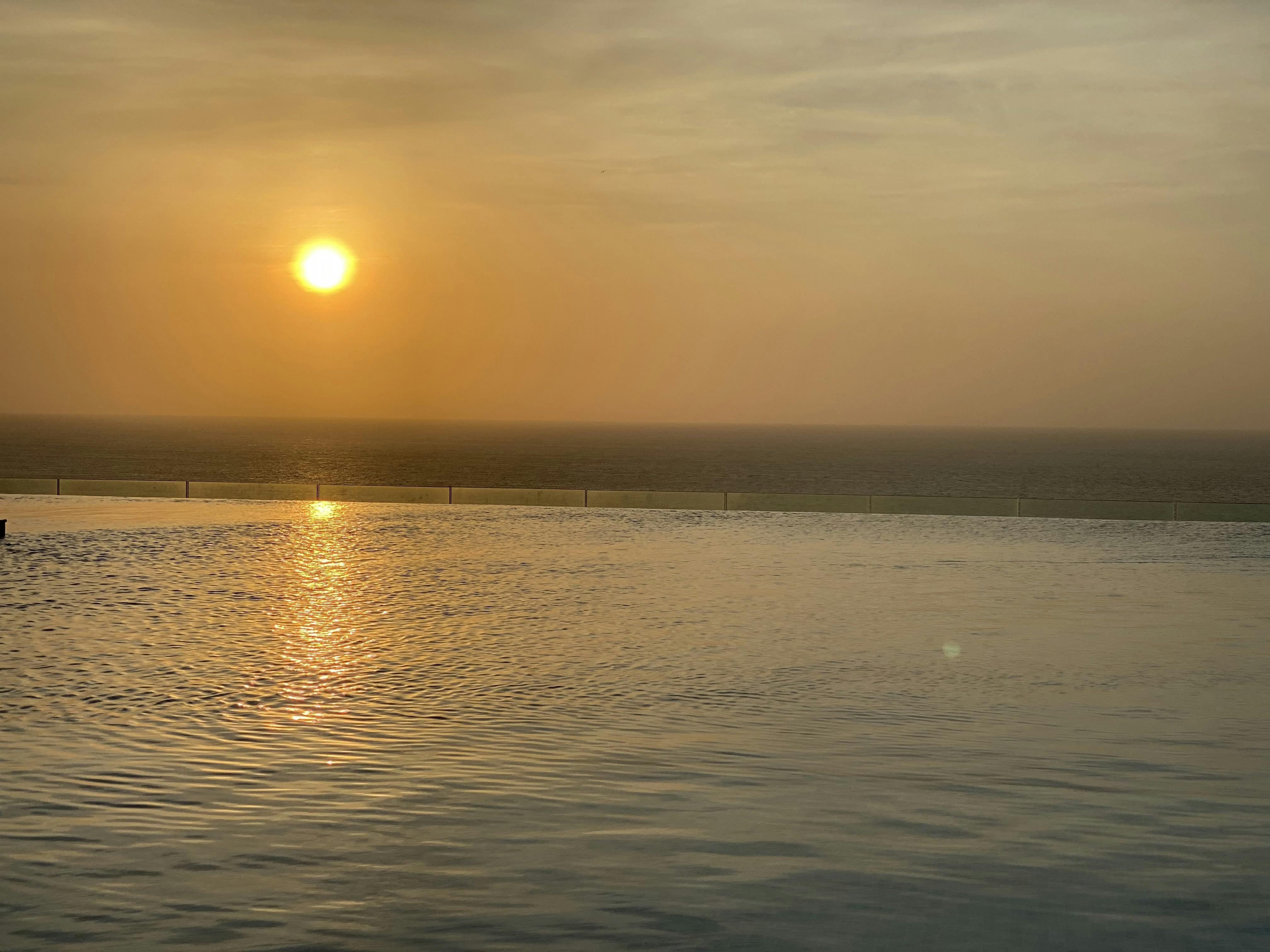 Luxurious hotel infinity pool at sunset, golden amber sky, calm water reflections, warm opulent atmosphere