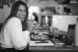 A smiling blogger typing on a laptop surrounded by delicious pastries and coffee.