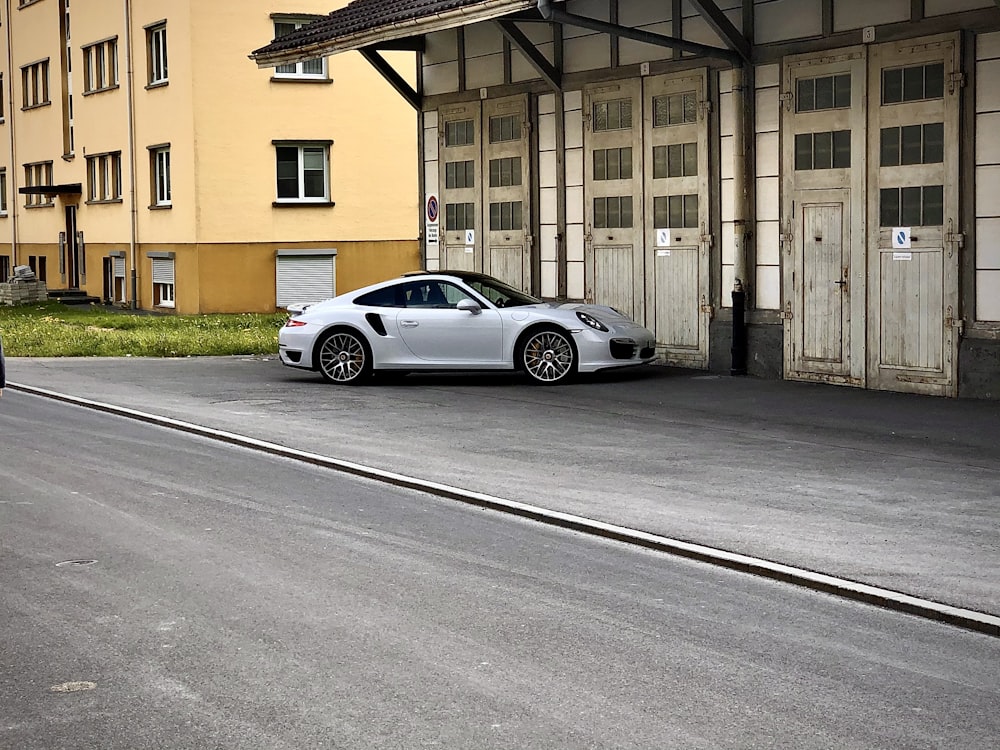 white coupe parked beside brown building during daytime