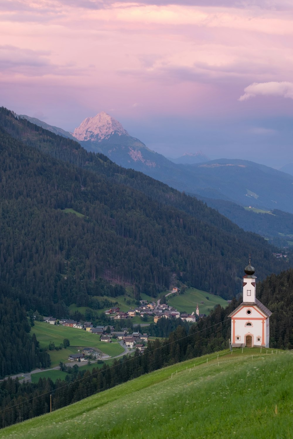 Weißes und schwarzes Betongebäude in der Nähe von grünen Bäumen und Bergen tagsüber