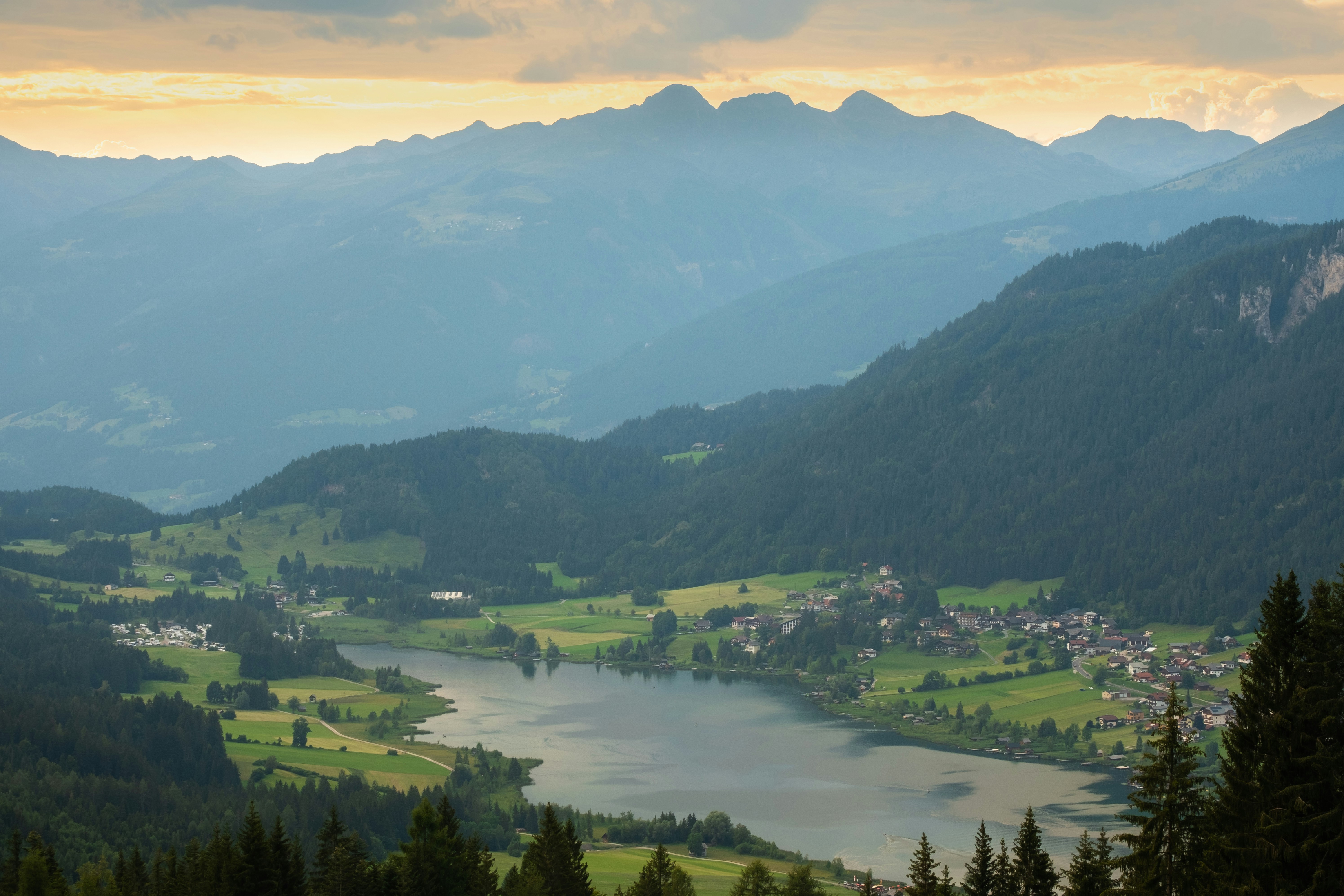 green mountains and green trees during daytime, A storm rolls in as the summer sun is setting over the alpine mountain lake Weissensee, Carinthia, Austria