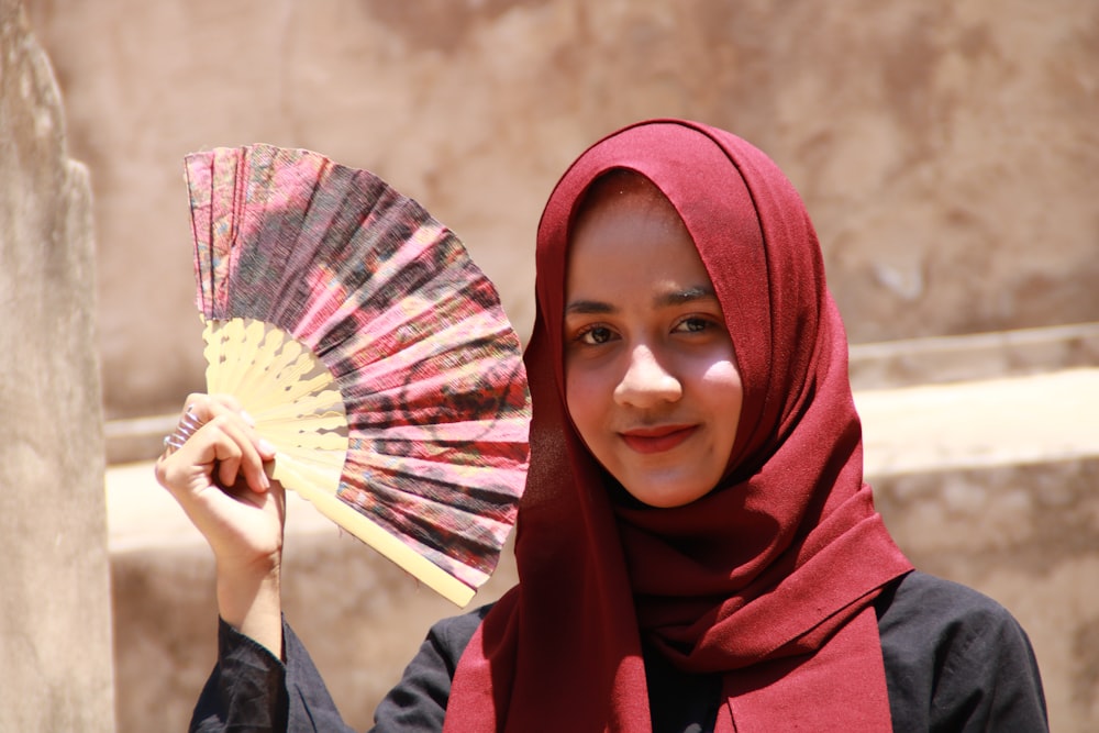 mulher no hijab vermelho segurando o ventilador da mão
