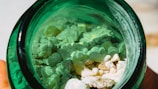 A close-up view of white and light green rocks or granules inside a dark green glass jar. The materials inside the jar appear rough and irregularly shaped, creating a textured appearance.