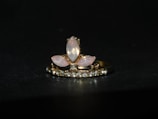 A gold ring adorned with a central arrangement of marquise-shaped moonstones, surrounded by a row of small sparkling diamonds. The setting features a combination of pink and clear stones against a dark background, highlighting the elegance of the jewelry.