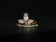 A gold ring adorned with a central arrangement of marquise-shaped moonstones, surrounded by a row of small sparkling diamonds. The setting features a combination of pink and clear stones against a dark background, highlighting the elegance of the jewelry.