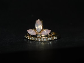 A gold ring adorned with a central arrangement of marquise-shaped moonstones, surrounded by a row of small sparkling diamonds. The setting features a combination of pink and clear stones against a dark background, highlighting the elegance of the jewelry.