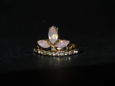 A gold ring adorned with a central arrangement of marquise-shaped moonstones, surrounded by a row of small sparkling diamonds. The setting features a combination of pink and clear stones against a dark background, highlighting the elegance of the jewelry.