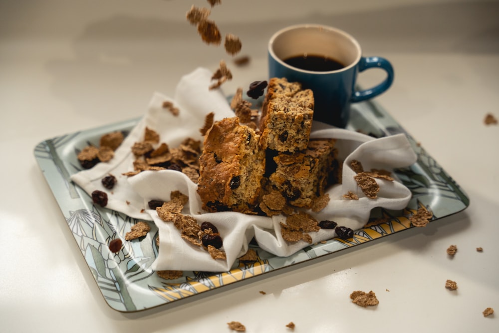 brown cookies on white ceramic plate beside blue ceramic mug