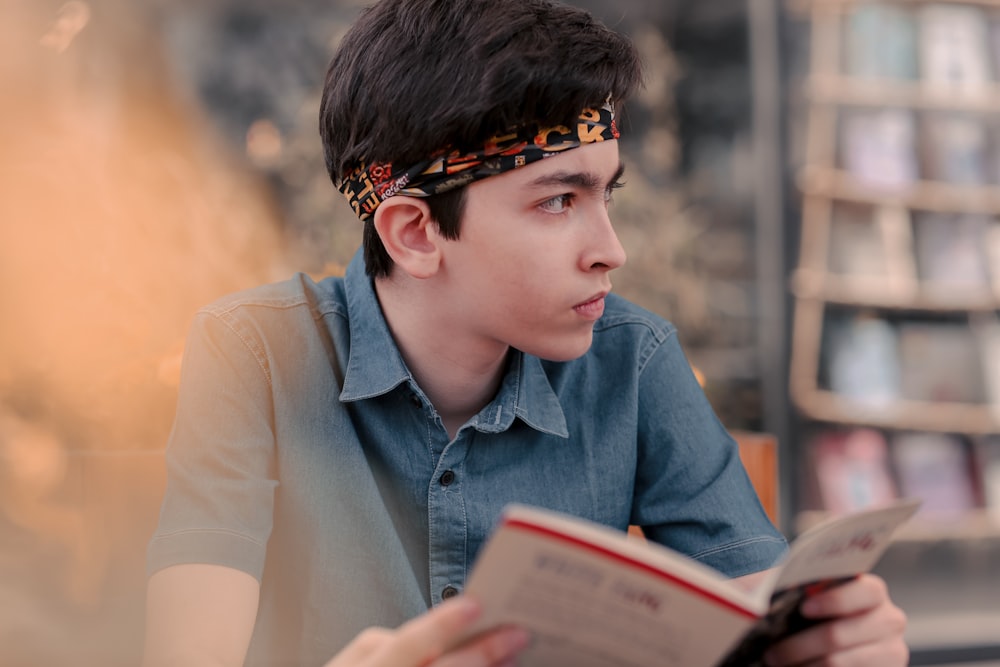 boy in blue denim button up shirt holding white book