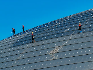 Technicians in safety gear inspecting a large commercial roof under clear skies.