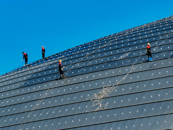 Technicians in safety gear inspecting a large commercial roof under clear skies.